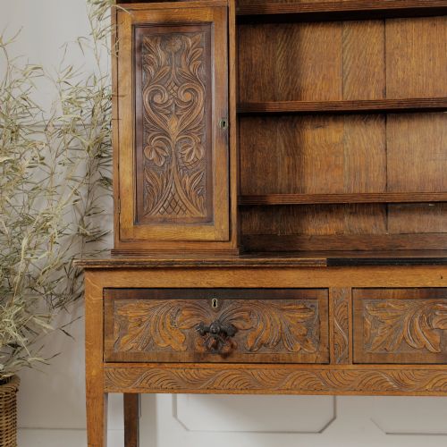 fig 2. A mid-19th-century carved oak dresser featuring three relief-carved drawers, two side cupboards, tapered legs, and an upper display rack with open shelving.