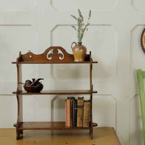 fig 1. A three-tier warm brown wooden wall shelving unit featuring shaped side supports, wedged tenons, and a carved pierced cresting pediment.