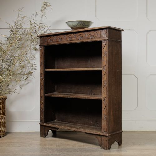fig 1. An early 20th-century dark oak open bookcase featuring a carved lunette frieze and three tiers of shelving.