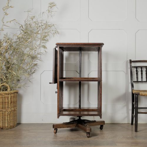 fig 1. An Edwardian dark oak revolving bookcase featuring vertical slats, multiple shelf tiers, an adjustable folding reading rest, and a quadruped base on castors.