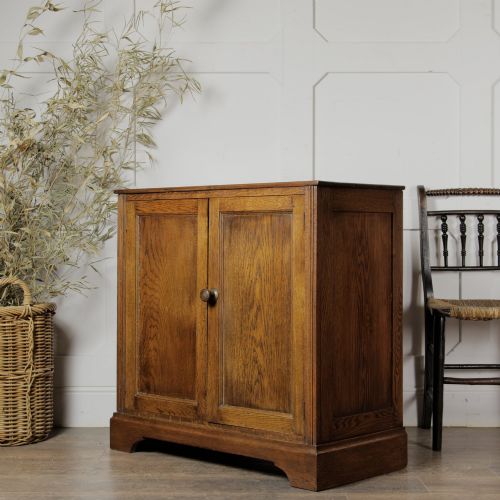 fig 1. A solid oak low cupboard featuring two panelled doors with a central wooden knob handle set on a shaped plinth base.