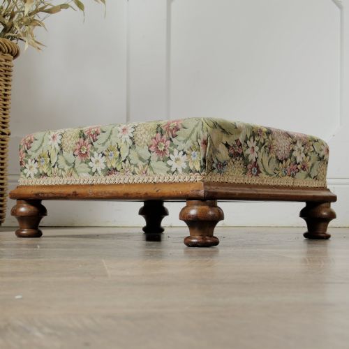 fig 1. A low Victorian square footstool with green floral tapestry upholstery, decorative braid trim, and turned mahogany feet.