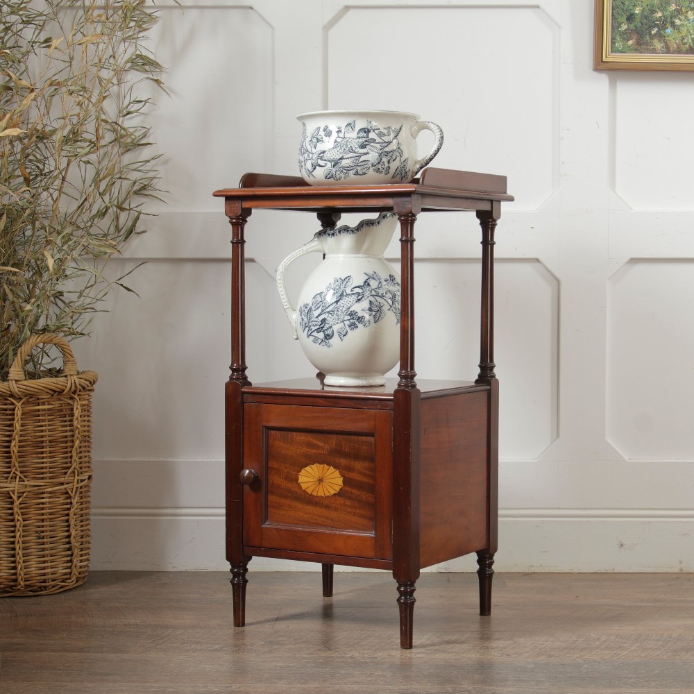 A Victorian mahogany pot cupboard with an open upper shelf supported by turned columns, sitting above a single-door cupboard adorned with a central marquetry inlay.