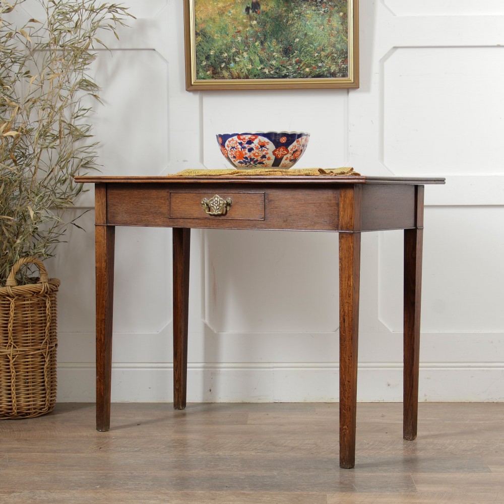 A George III Georgian oak side table featuring a single drawer with a brass handle plate and four square tapered legs.