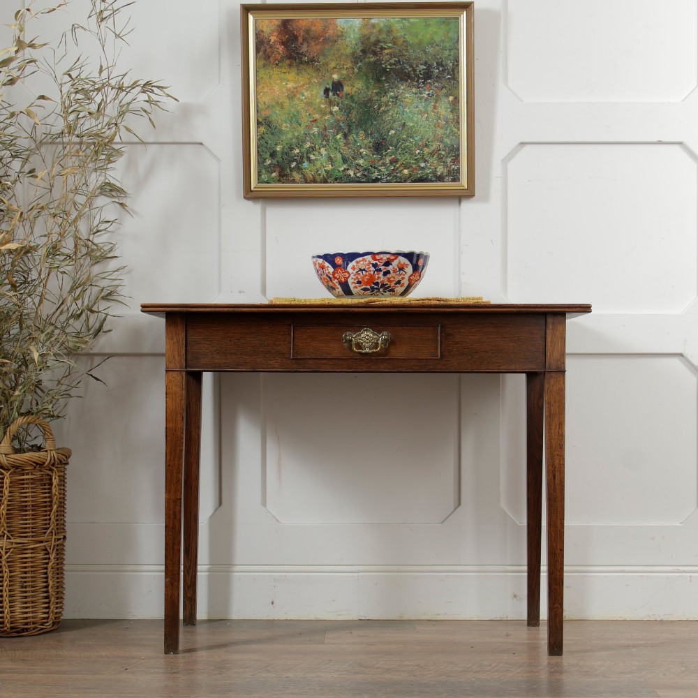A George III Georgian oak side table featuring a single drawer with a brass handle plate and four square tapered legs. View II