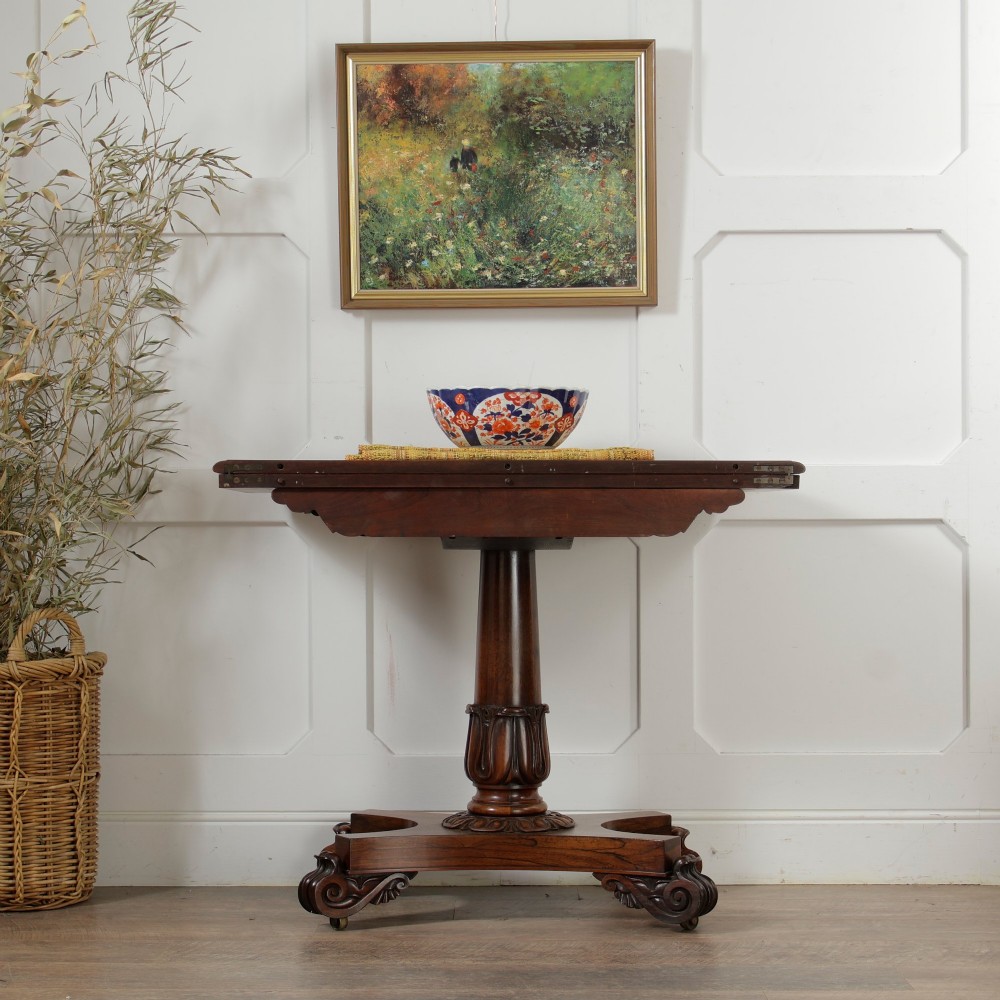 A William IV dark rosewood card table featuring a pedestal stem, carved scroll feet on castors, and a gadrooned top edge. View IV