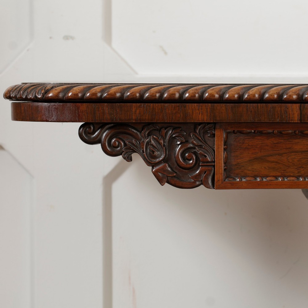 A William IV dark rosewood card table featuring a pedestal stem, carved scroll feet on castors, and a gadrooned top edge. View VIII