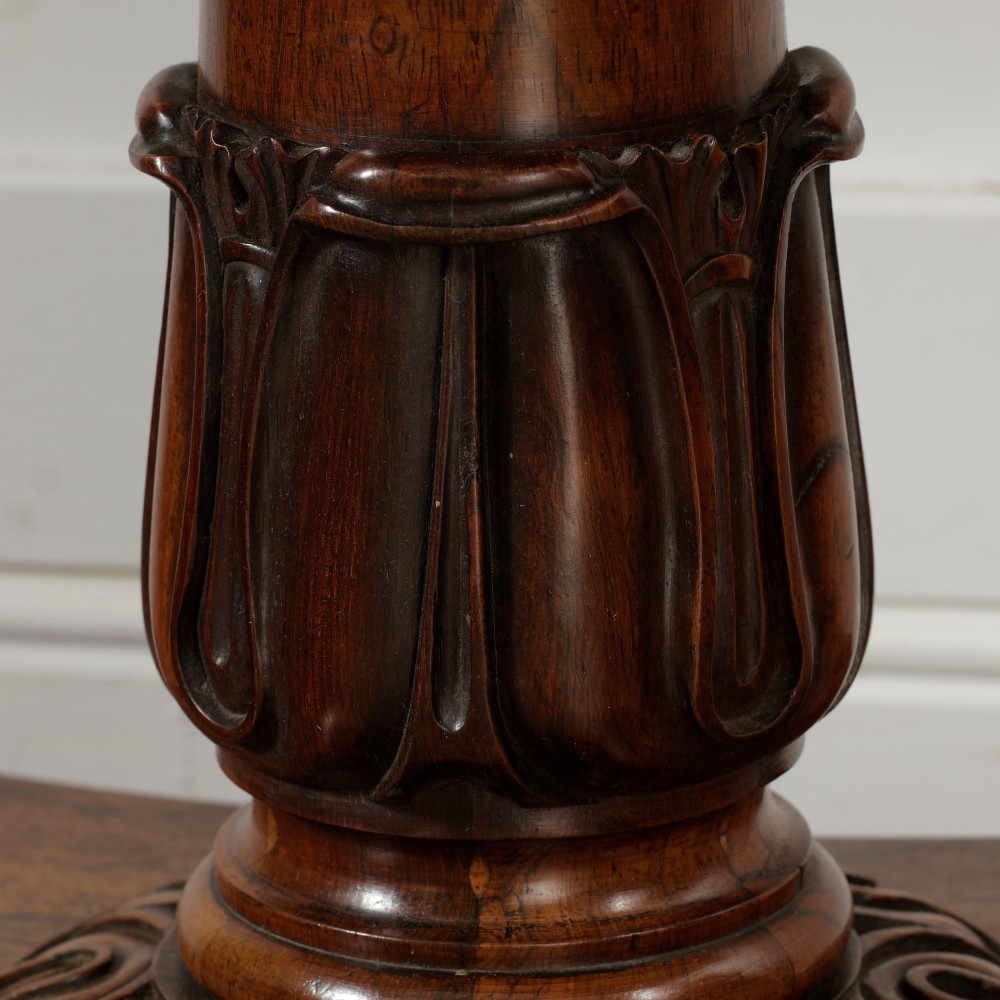 A William IV dark rosewood card table featuring a pedestal stem, carved scroll feet on castors, and a gadrooned top edge. View X