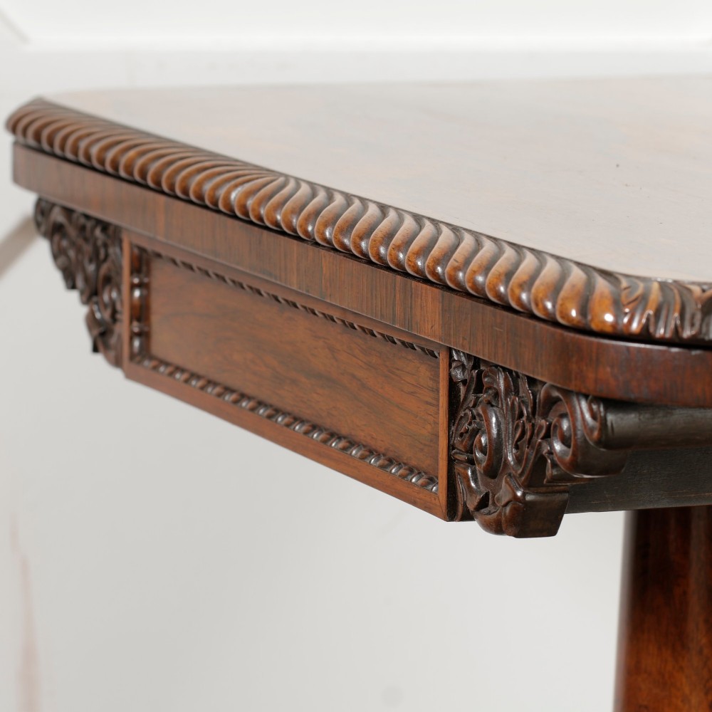A William IV dark rosewood card table featuring a pedestal stem, carved scroll feet on castors, and a gadrooned top edge. View XIII