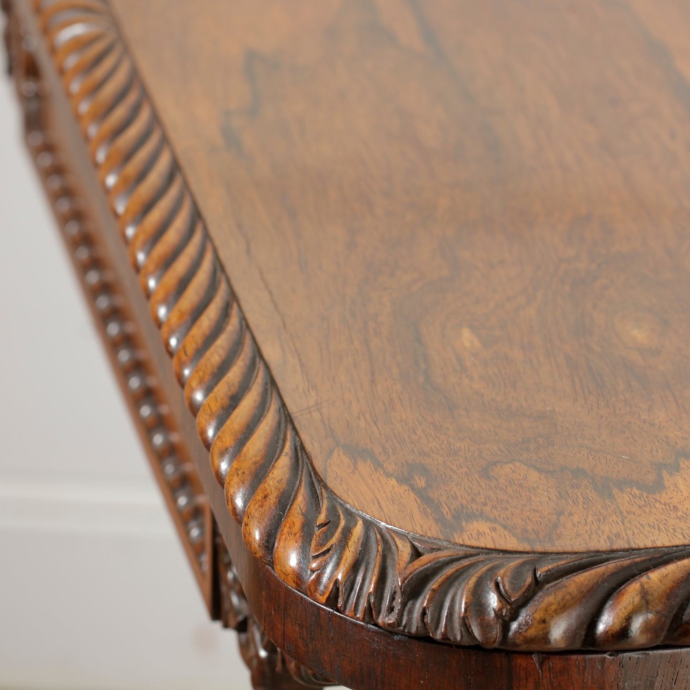 A William IV dark rosewood card table featuring a pedestal stem, carved scroll feet on castors, and a gadrooned top edge. View XIV