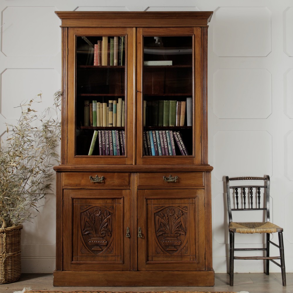 A late Victorian wooden glazed bookcase featuring two upper glass doors above two drawers and a double-door cupboard carved with floral urn motifs. View II