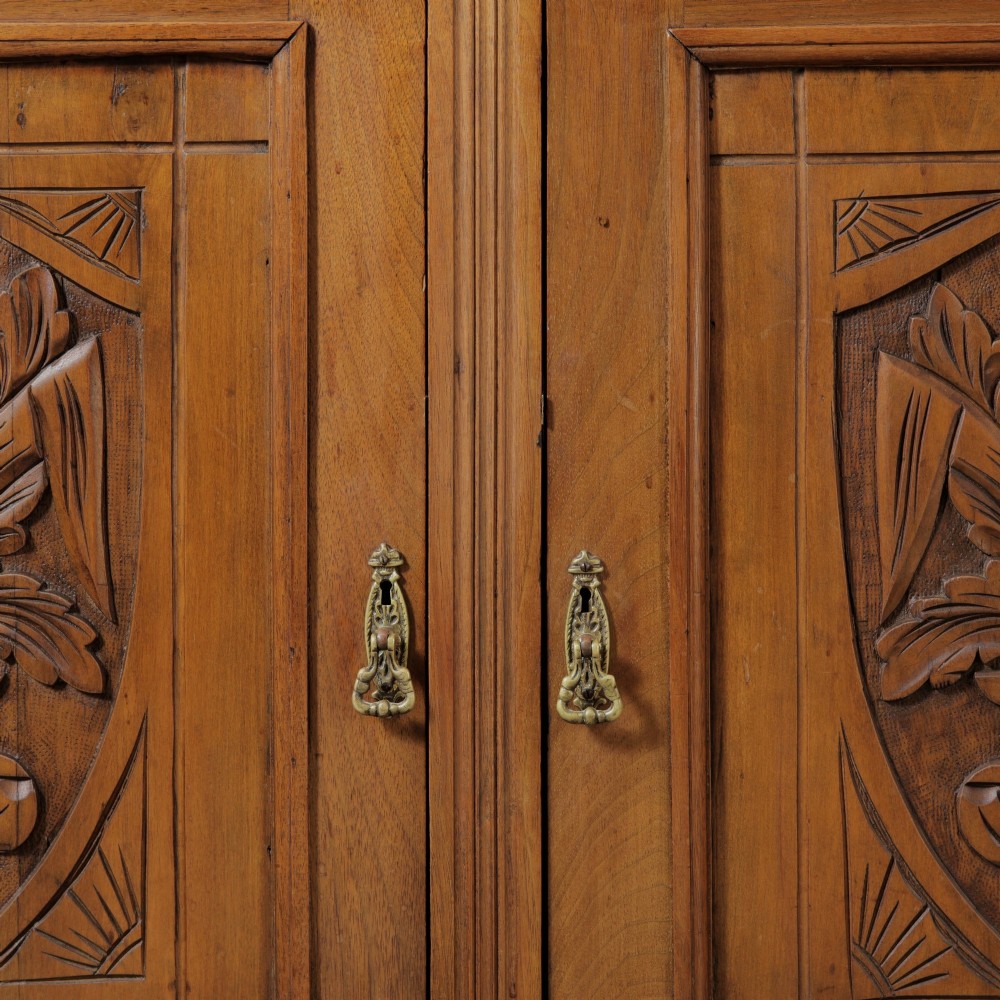 A late Victorian wooden glazed bookcase featuring two upper glass doors above two drawers and a double-door cupboard carved with floral urn motifs. View V