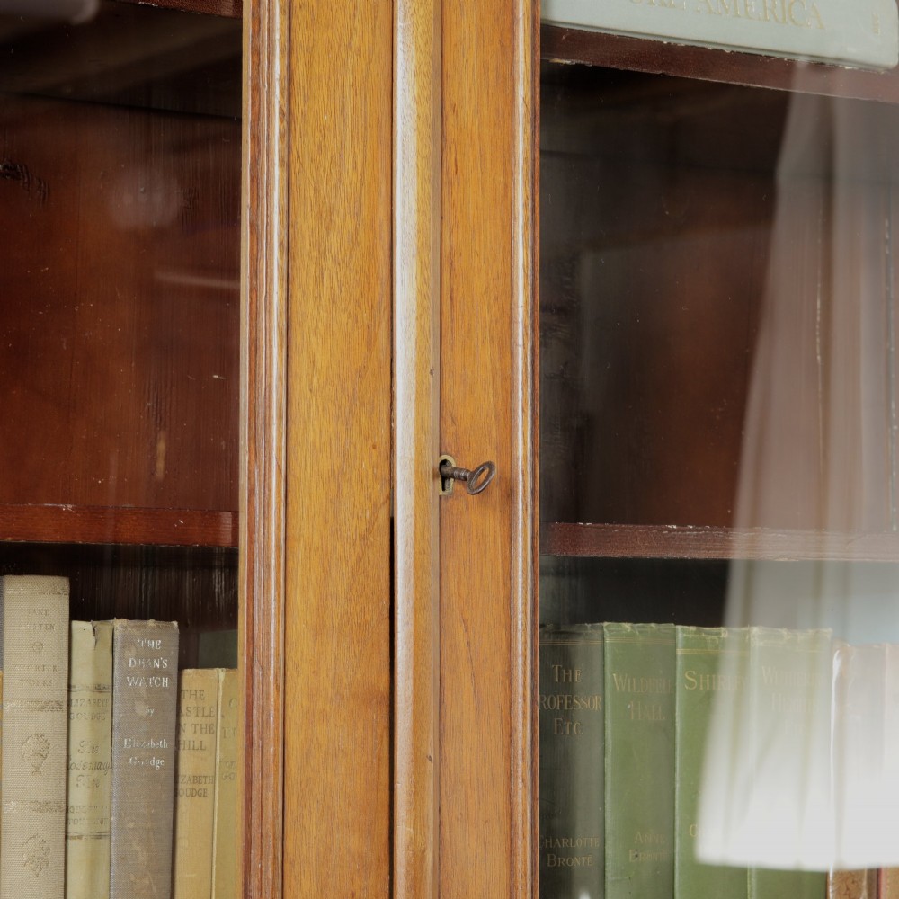 A late Victorian wooden glazed bookcase featuring two upper glass doors above two drawers and a double-door cupboard carved with floral urn motifs. View X