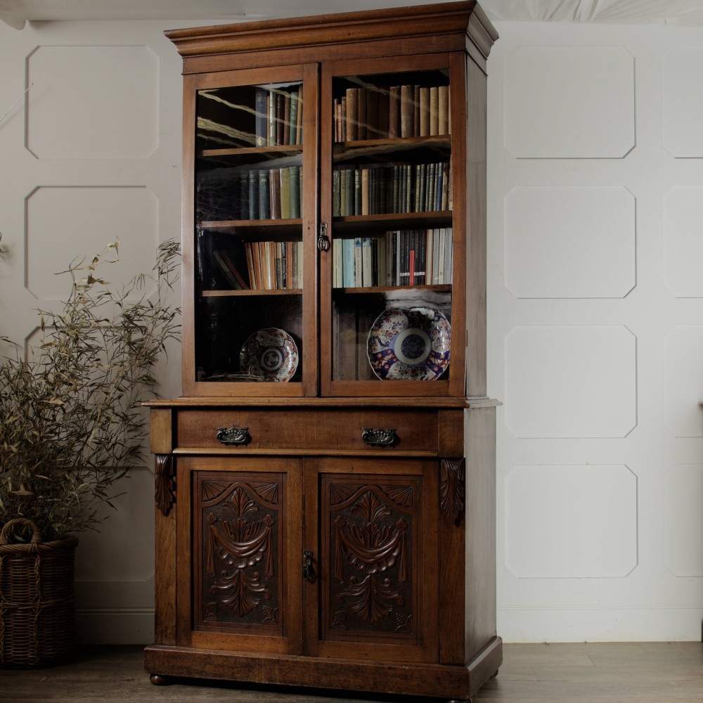 A mid-Victorian mahogany bookcase featuring a two-door glazed upper section, a single frieze drawer, and a lower cupboard with carved panel doors.