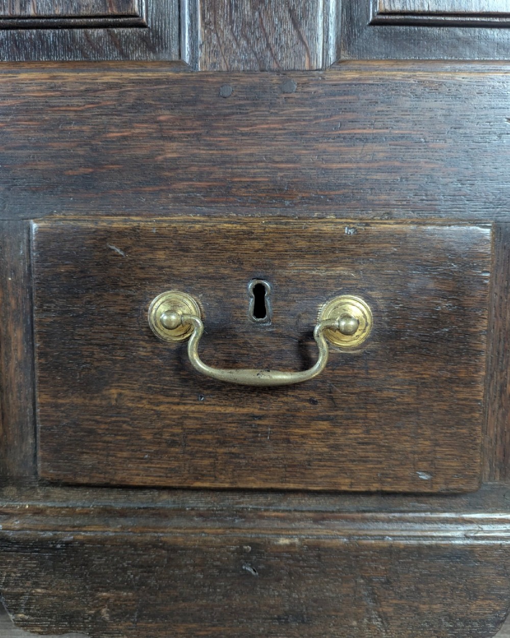 An 18th-century dark oak mule chest featuring four fielded front panels above three small drawers with brass handles. View IX