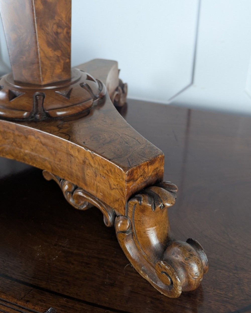 An antique William IV figured walnut revolving piano stool featuring an olive green upholstered square seat, a faceted column, and a carved triform base with scroll feet. View VII