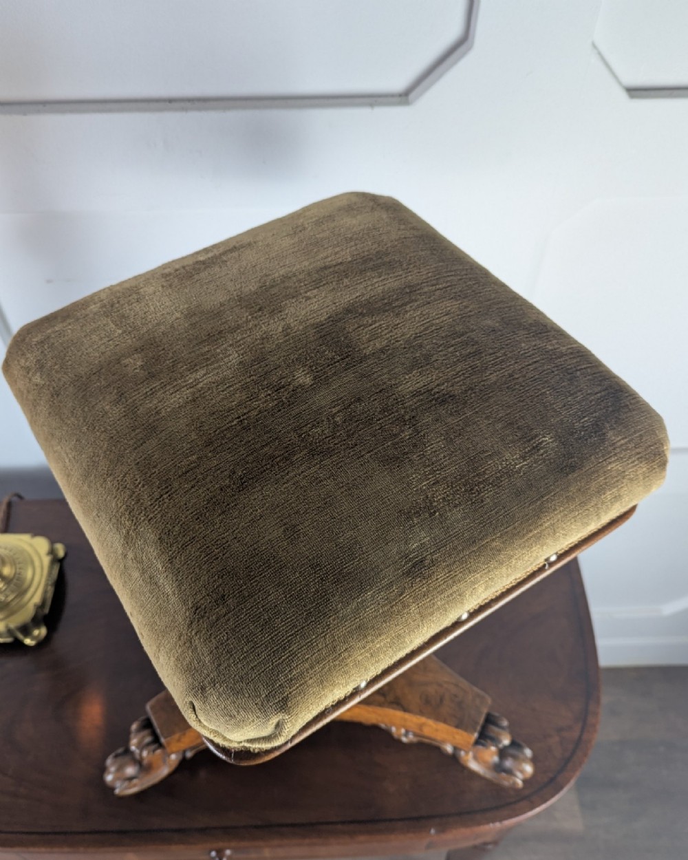 An antique William IV figured walnut revolving piano stool featuring an olive green upholstered square seat, a faceted column, and a carved triform base with scroll feet. View XI