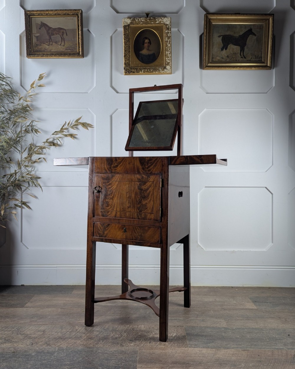A Georgian Cuban mahogany fold-away washstand featuring an upright mirror, opened side leaves, a central cupboard, a lower drawer, and an X-frame stretcher.