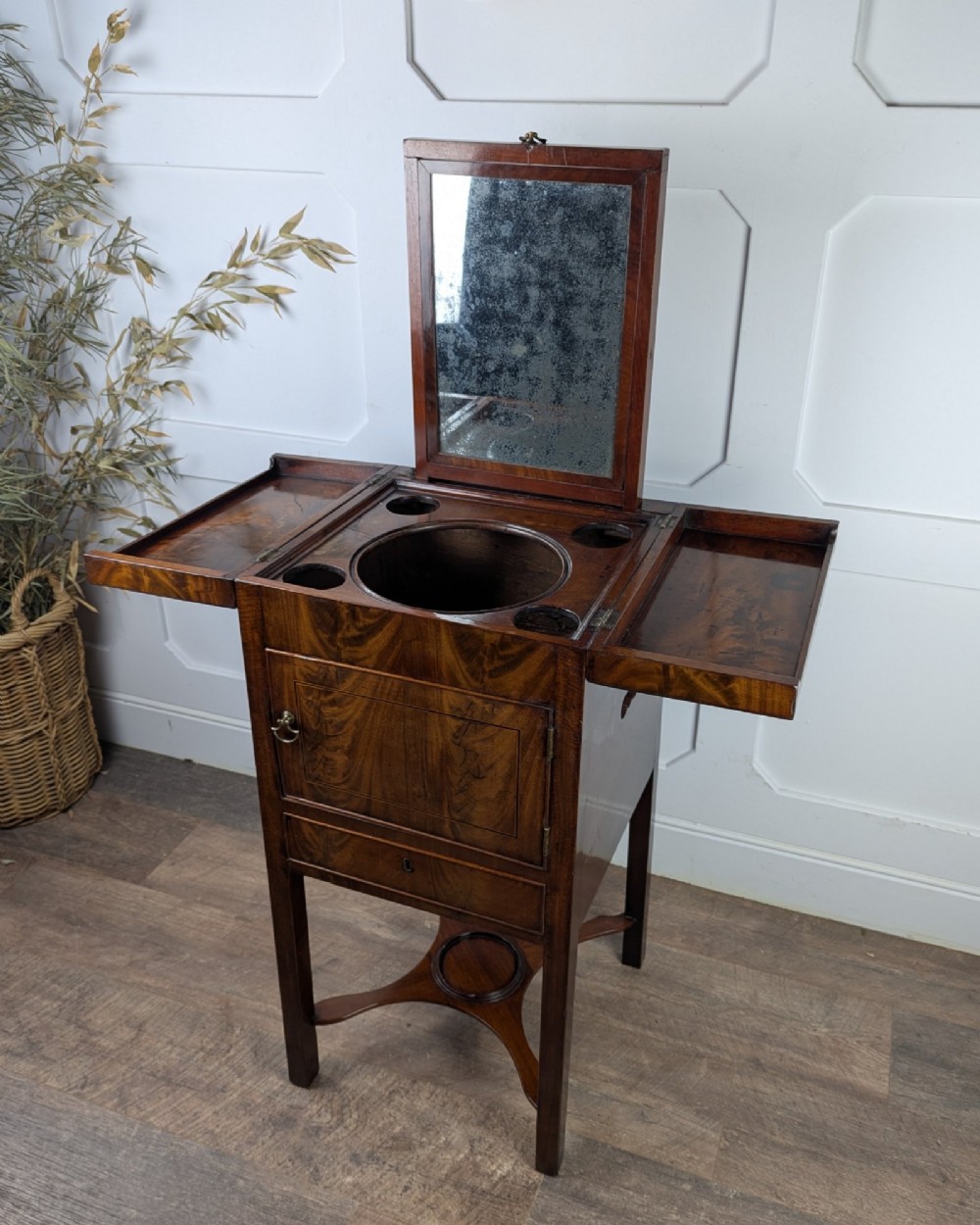 A Georgian Cuban mahogany fold-away washstand featuring an upright mirror, opened side leaves, a central cupboard, a lower drawer, and an X-frame stretcher. View IV