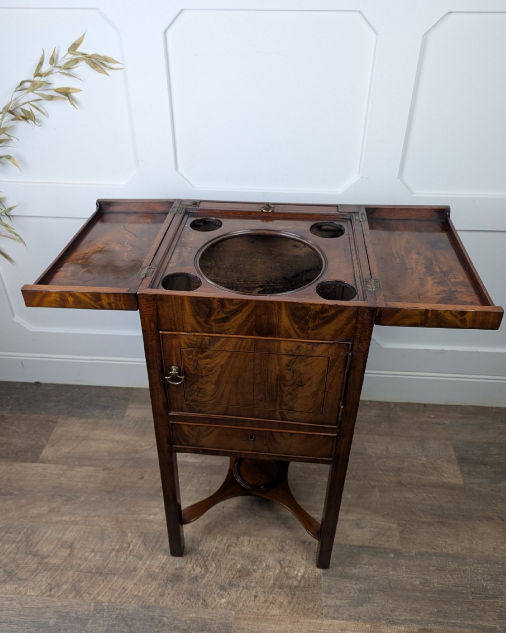 A Georgian Cuban mahogany fold-away washstand featuring an upright mirror, opened side leaves, a central cupboard, a lower drawer, and an X-frame stretcher. View X