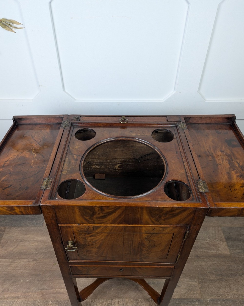 A Georgian Cuban mahogany fold-away washstand featuring an upright mirror, opened side leaves, a central cupboard, a lower drawer, and an X-frame stretcher. View XI