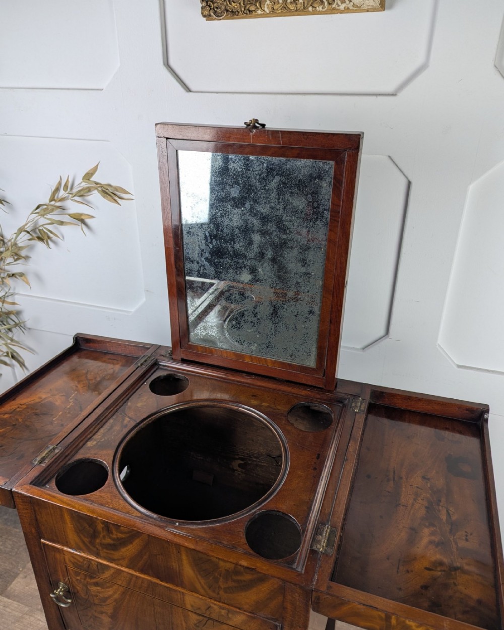 A Georgian Cuban mahogany fold-away washstand featuring an upright mirror, opened side leaves, a central cupboard, a lower drawer, and an X-frame stretcher. View XII