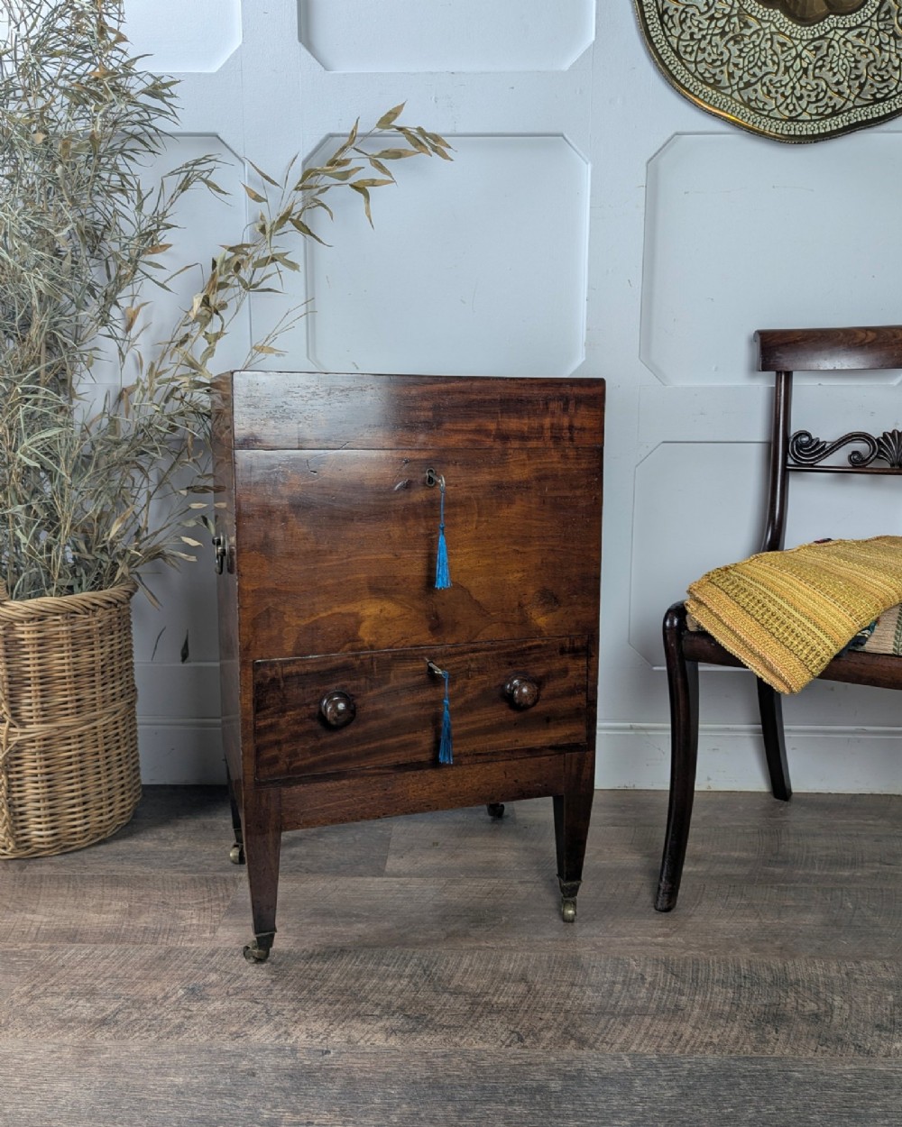 A Georgian dark mahogany cellarette featuring a hinged top lid, a lower drawer with wooden turned knobs, brass side handles, and square tapered legs on brass castors.