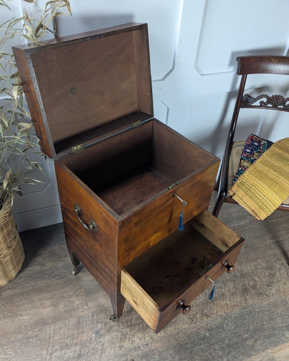 A Georgian dark mahogany cellarette featuring a hinged top lid, a lower drawer with wooden turned knobs, brass side handles, and square tapered legs on brass castors. View VII