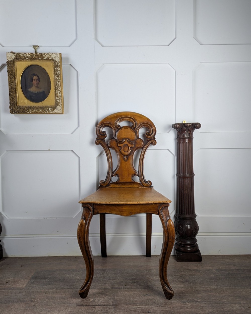 A Victorian carved solid oak hall chair featuring an openwork shield back, a solid timber seat, and shaped cabriole front legs. View V