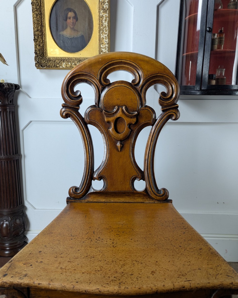 A Victorian carved solid oak hall chair featuring an openwork shield back, a solid timber seat, and shaped cabriole front legs. View IX