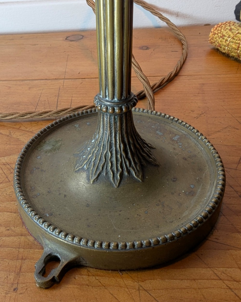 A slim early 20th-century aged brass lamp featuring a fluted stem, circular base, socket switch, and an exposed filament bulb. View VIII
