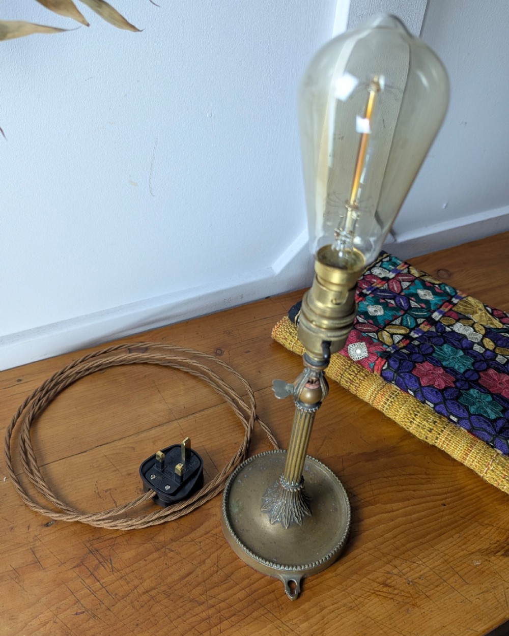 A slim early 20th-century aged brass lamp featuring a fluted stem, circular base, socket switch, and an exposed filament bulb. View IX