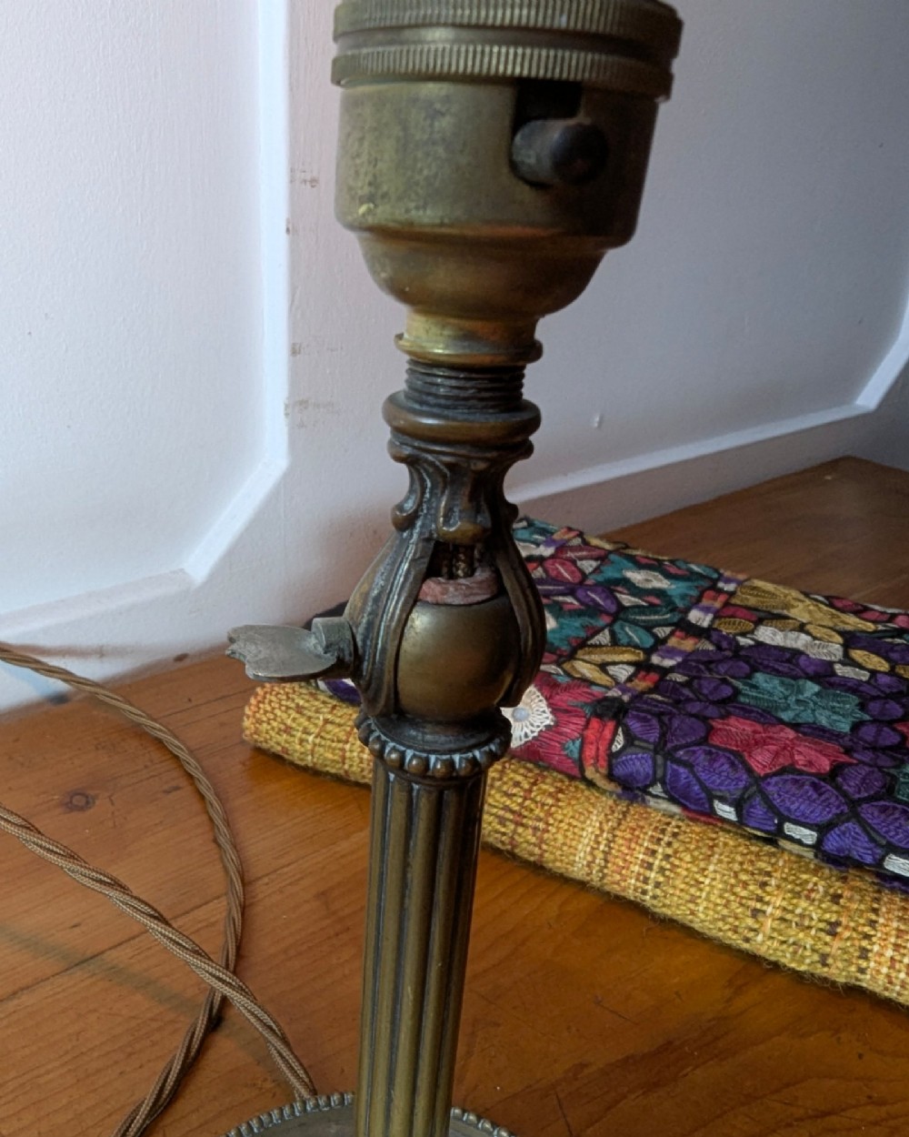 A slim early 20th-century aged brass lamp featuring a fluted stem, circular base, socket switch, and an exposed filament bulb. View X