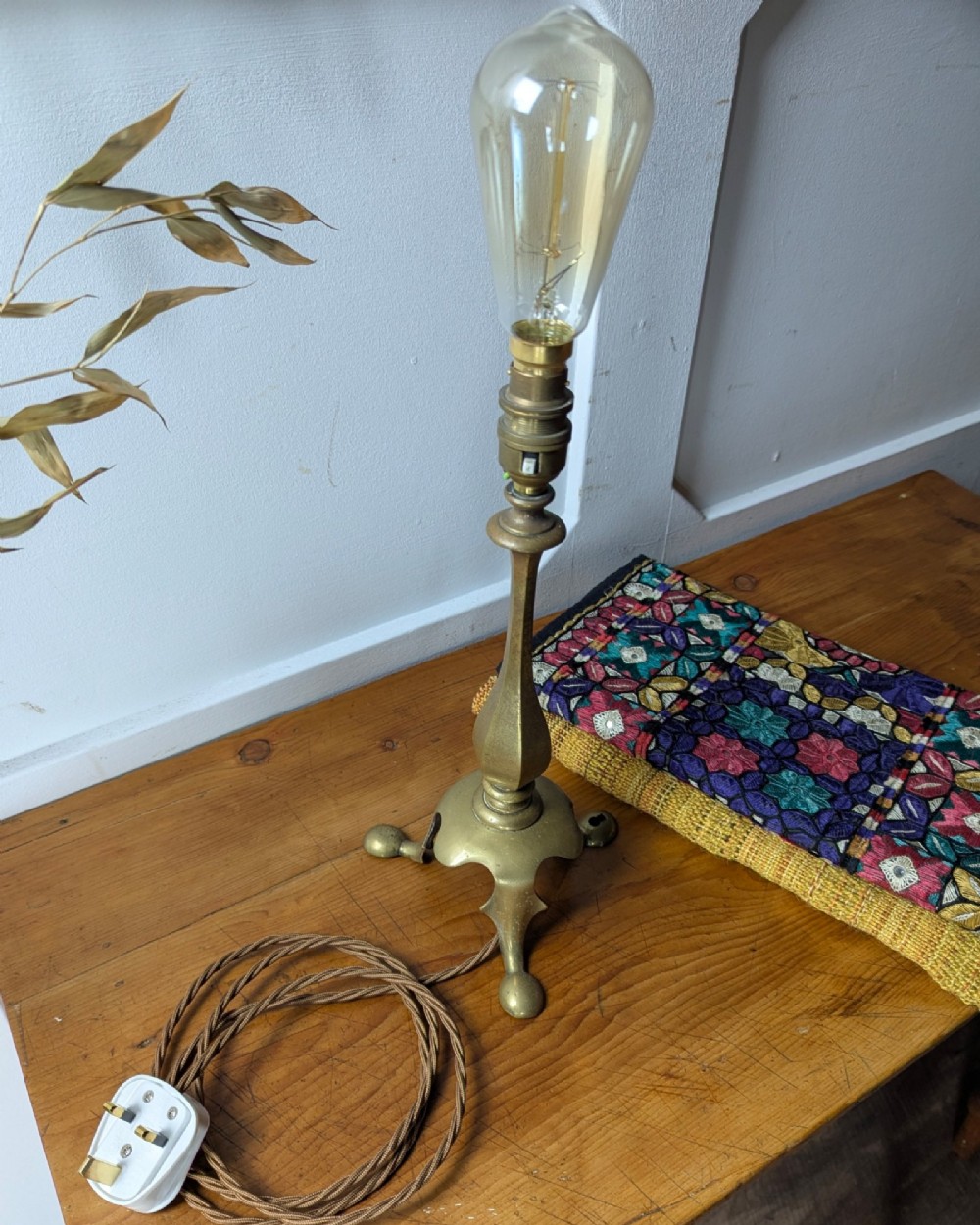 An antique brass table lamp featuring a hexagonal baluster stem resting on a three-legged cast base. View VII