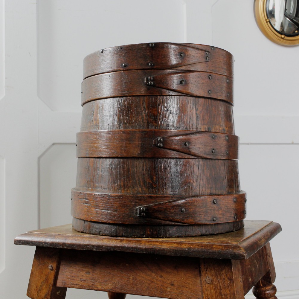 A cylindrical early 19th-century dark oak grain bin with bound wooden hoops, metal rivets, and a fitted lid. View III