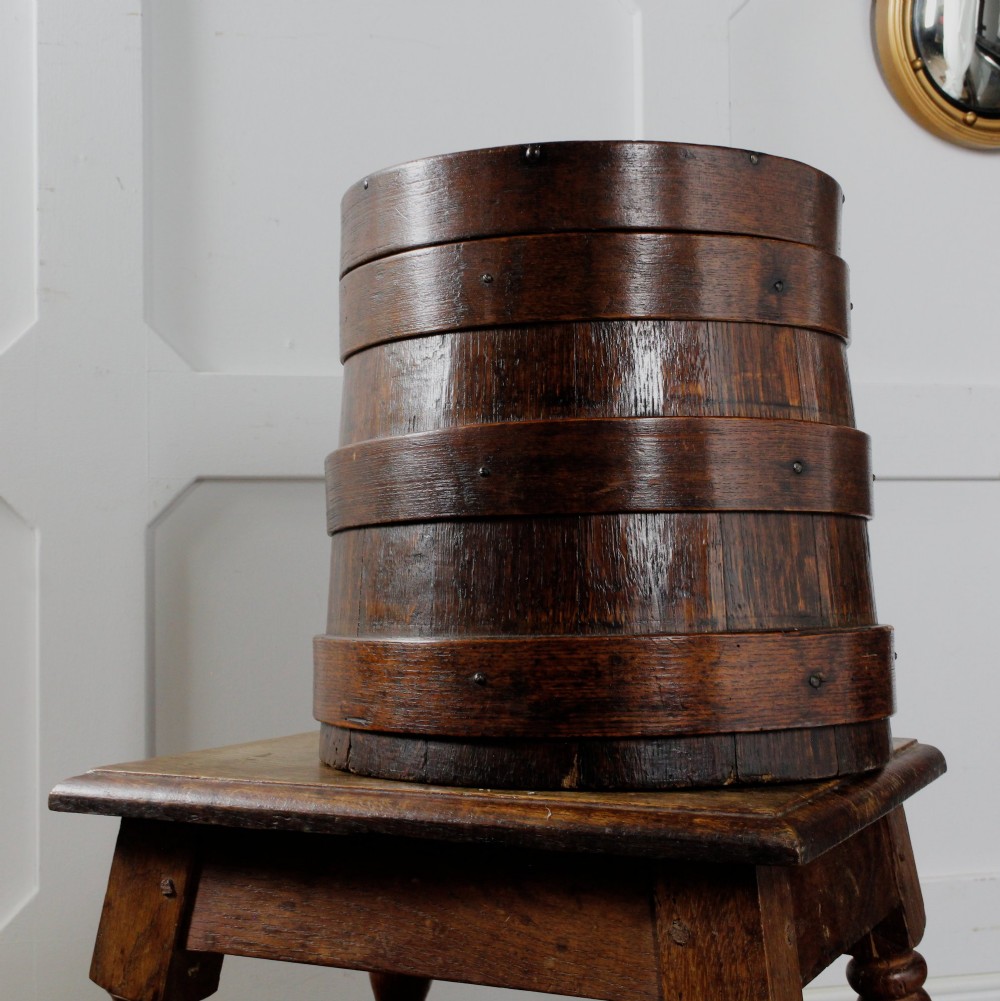 A cylindrical early 19th-century dark oak grain bin with bound wooden hoops, metal rivets, and a fitted lid. View IV