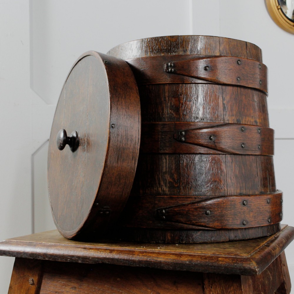A cylindrical early 19th-century dark oak grain bin with bound wooden hoops, metal rivets, and a fitted lid. View V