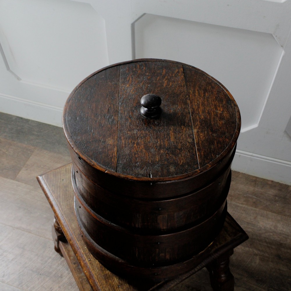 A cylindrical early 19th-century dark oak grain bin with bound wooden hoops, metal rivets, and a fitted lid. View VI