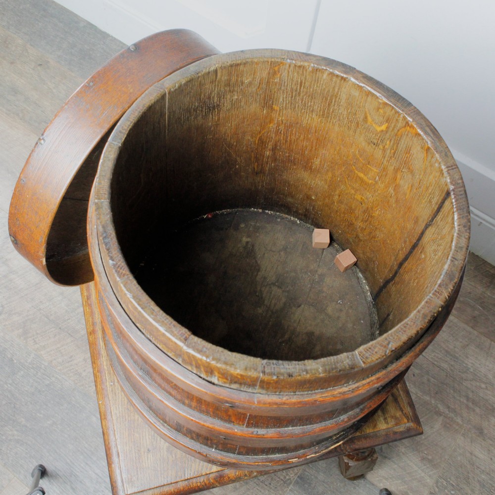 A cylindrical early 19th-century dark oak grain bin with bound wooden hoops, metal rivets, and a fitted lid. View VII