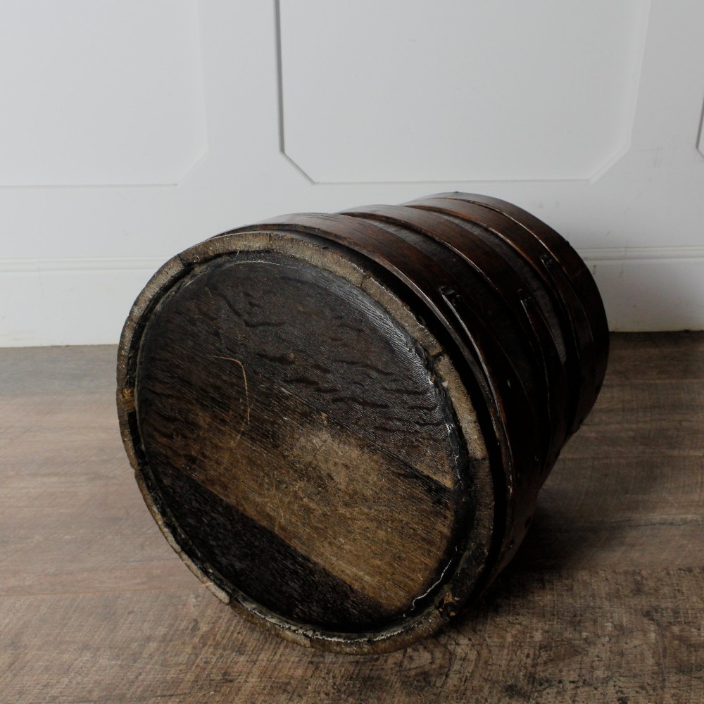 A cylindrical early 19th-century dark oak grain bin with bound wooden hoops, metal rivets, and a fitted lid. View VIII