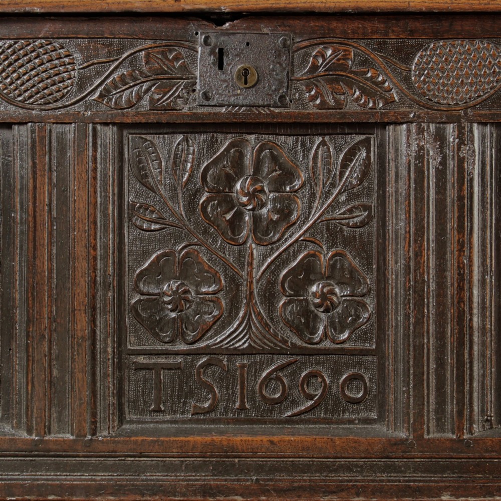 A dark oak panelled chest featuring detailed floral and foliage relief carvings, a central panel inscribed TS 1690, and an iron lockplate. View II