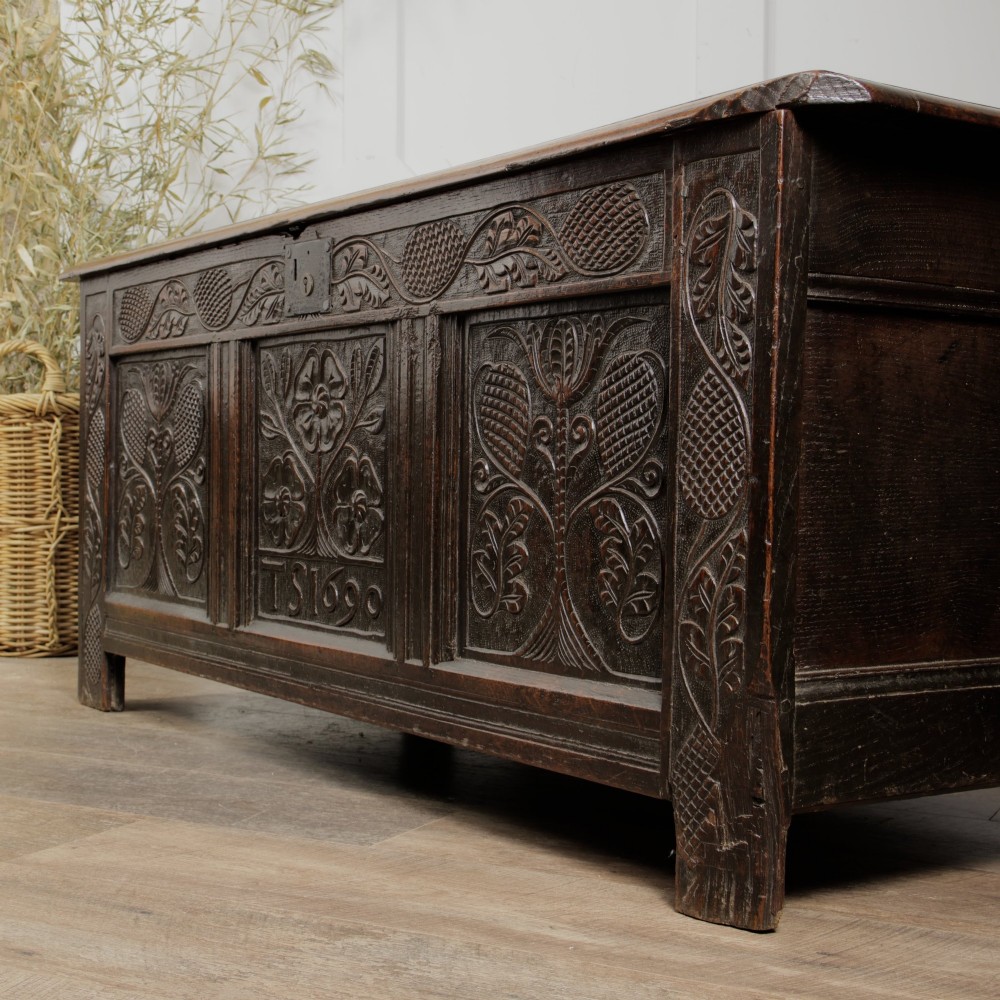 A dark oak panelled chest featuring detailed floral and foliage relief carvings, a central panel inscribed TS 1690, and an iron lockplate. View III