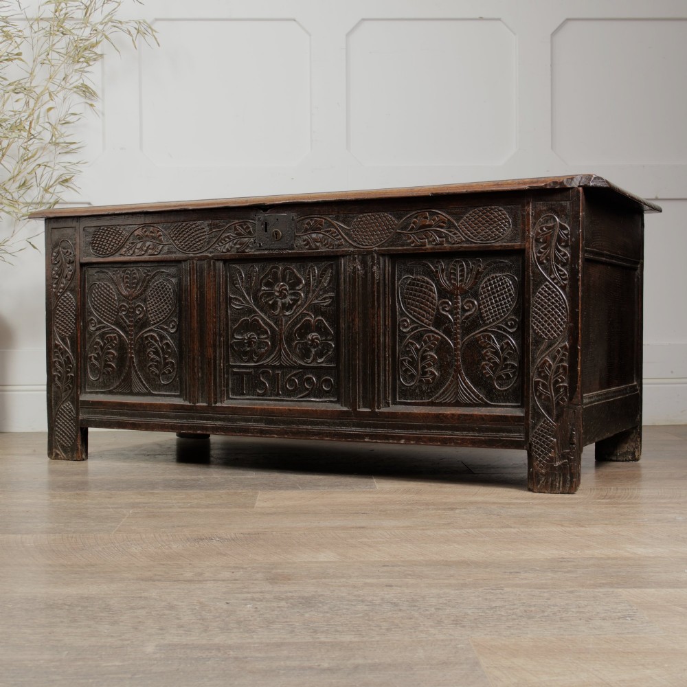 A dark oak panelled chest featuring detailed floral and foliage relief carvings, a central panel inscribed TS 1690, and an iron lockplate.
