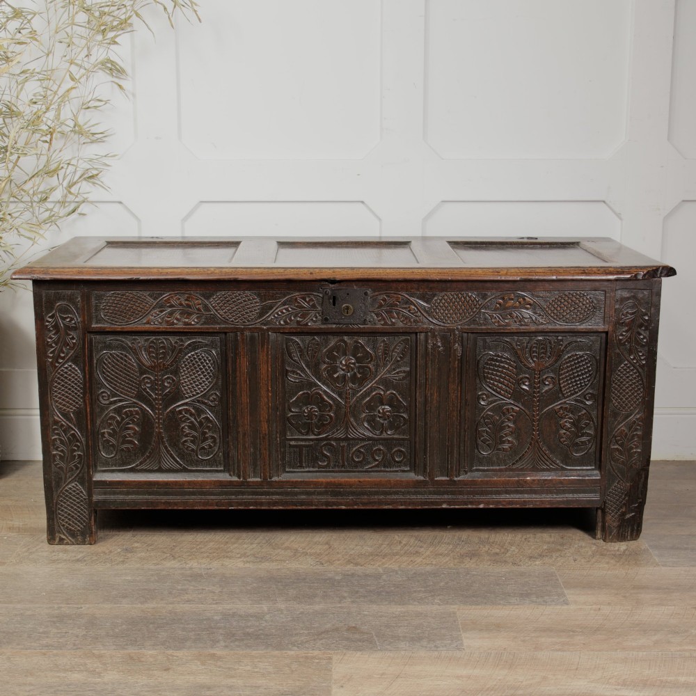 A dark oak panelled chest featuring detailed floral and foliage relief carvings, a central panel inscribed TS 1690, and an iron lockplate. View IV