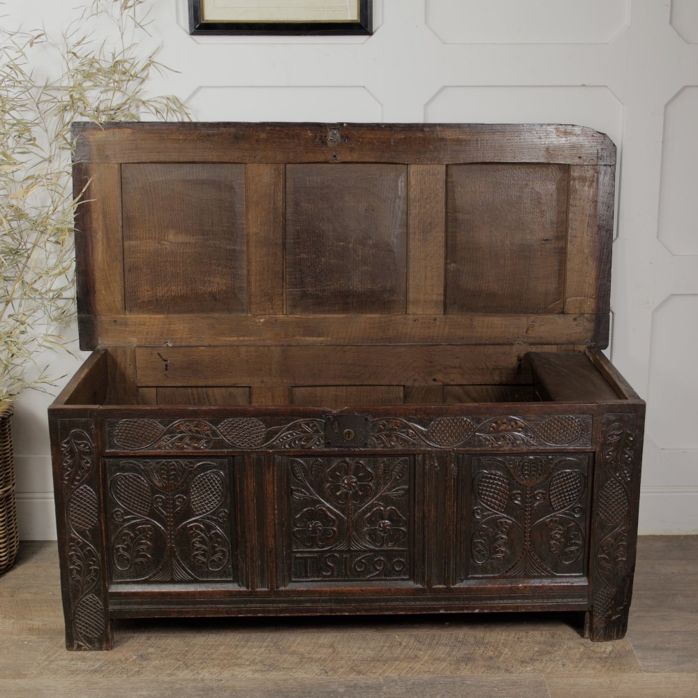 A dark oak panelled chest featuring detailed floral and foliage relief carvings, a central panel inscribed TS 1690, and an iron lockplate. View IX