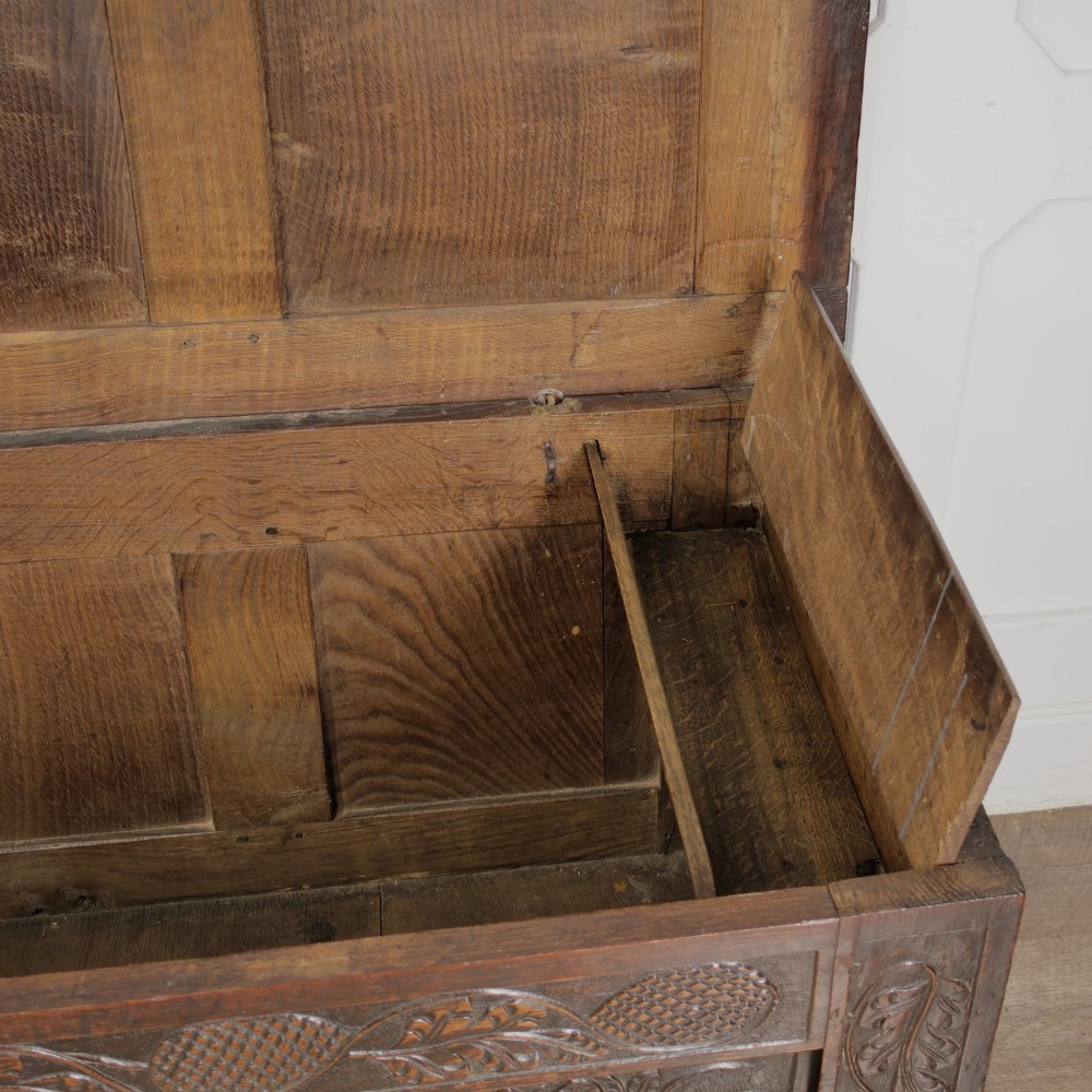 A dark oak panelled chest featuring detailed floral and foliage relief carvings, a central panel inscribed TS 1690, and an iron lockplate. View X