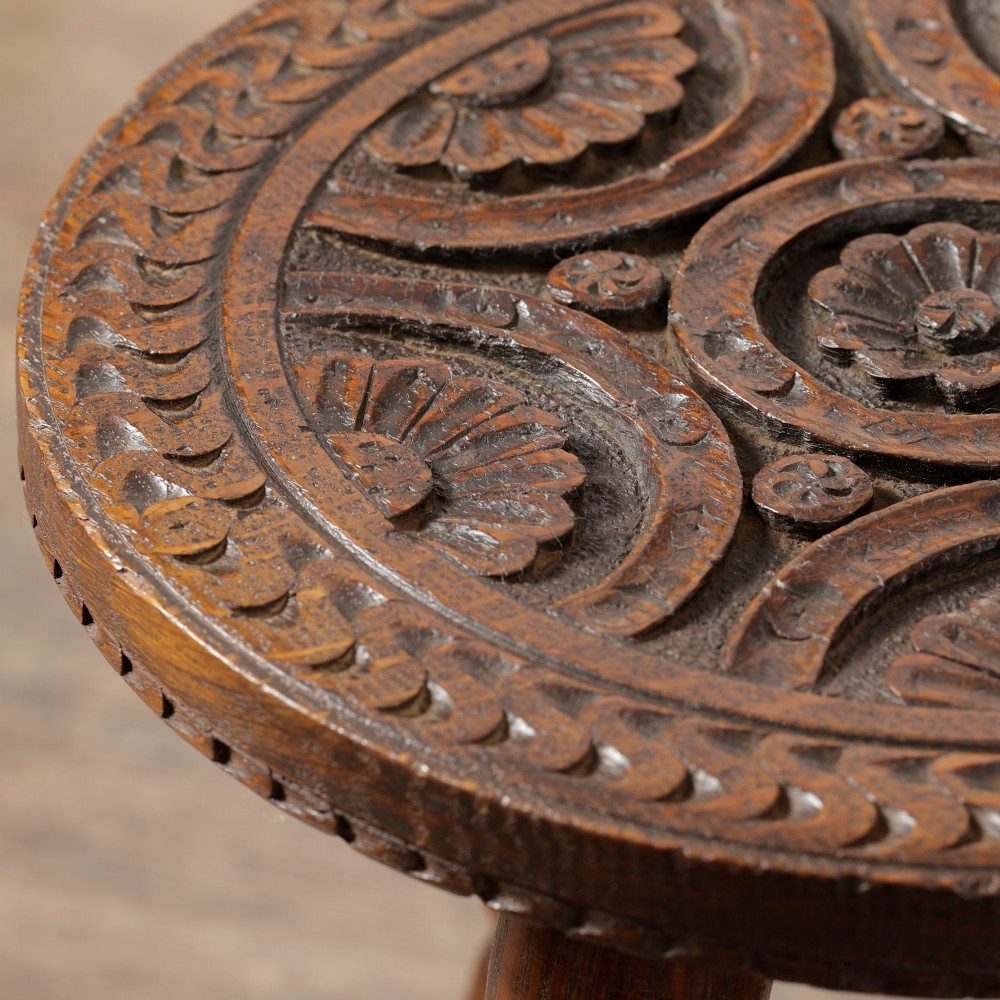 An early twentieth-century dark oak three-legged milking stool featuring turned legs and a carved round seat. View II