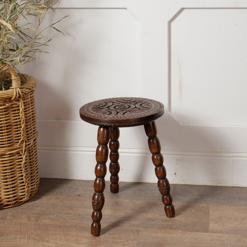 An early twentieth-century dark oak three-legged milking stool featuring turned legs and a carved round seat. View V