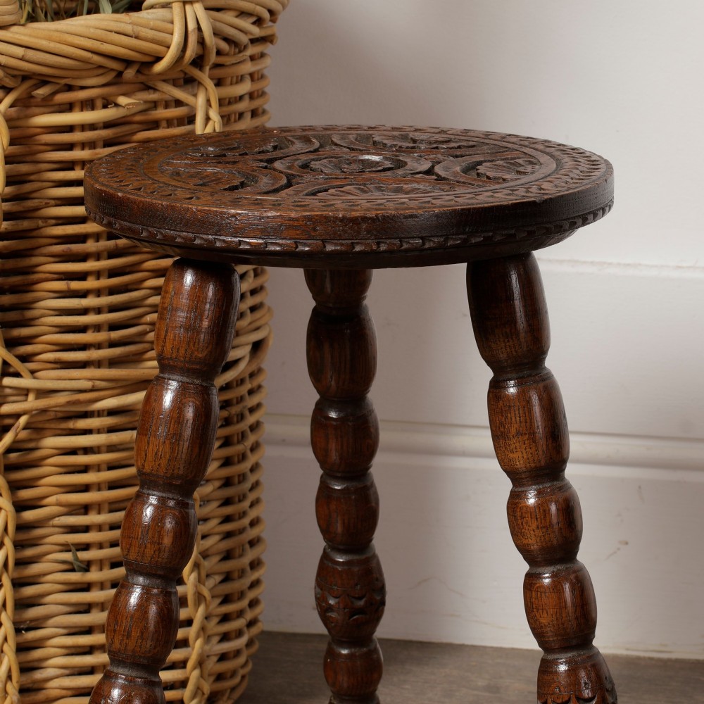 An early twentieth-century dark oak three-legged milking stool featuring turned legs and a carved round seat. View VII
