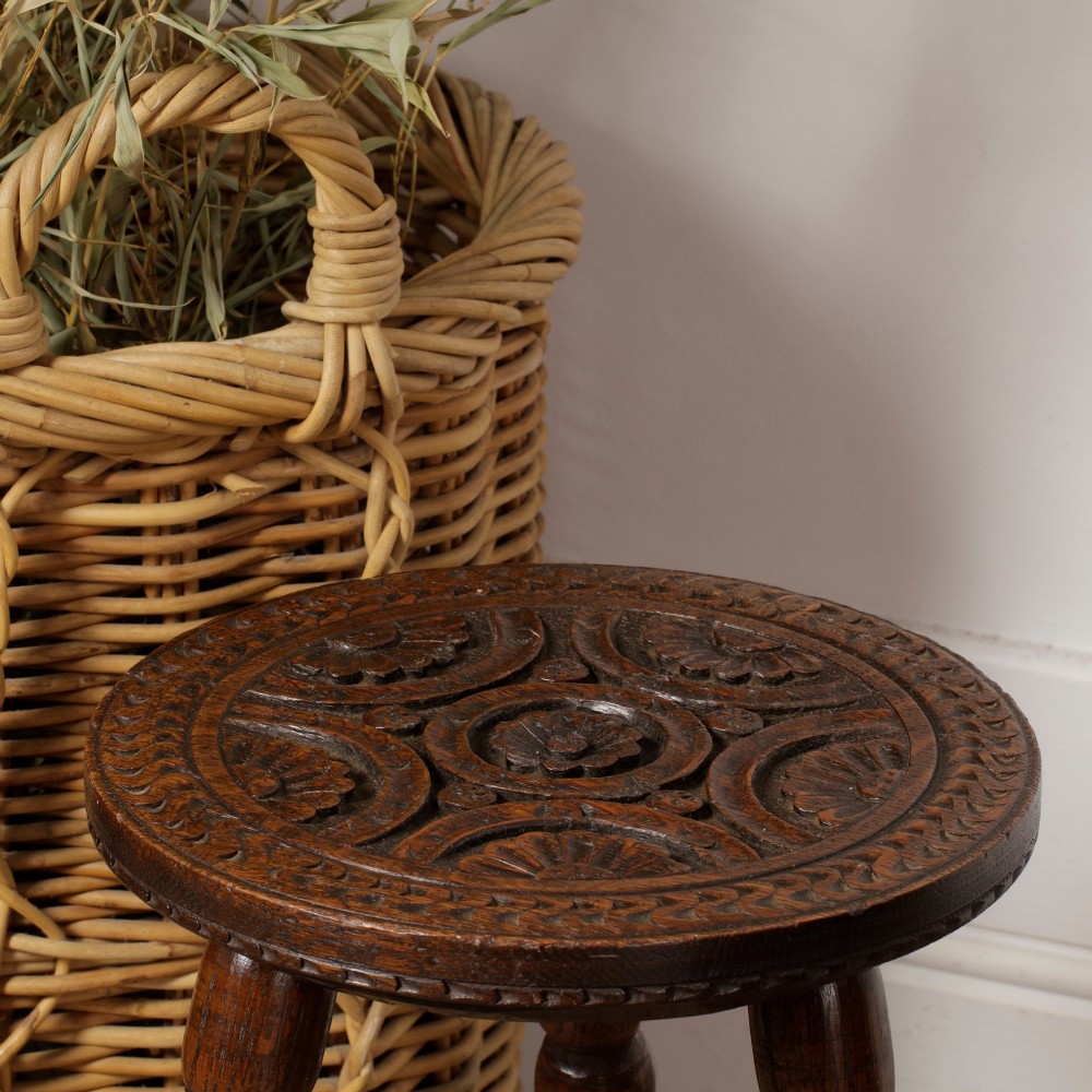 An early twentieth-century dark oak three-legged milking stool featuring turned legs and a carved round seat. View VIII